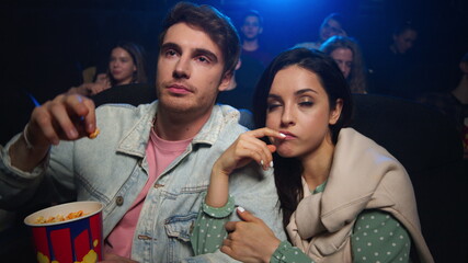 Romantic couple surprising in cinema. Young man eating popcorn in dark hall.