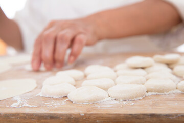 Small dough scattered on the cutting board and hands making dumplings in the background