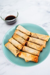 plant-based food, vegan homemade spring rolls with stir fried vegetables filling on blue plate next to soy sauce