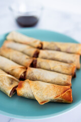 plant-based food, vegan homemade spring rolls with stir fried vegetables filling on blue plate next to soy sauce