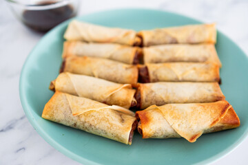 plant-based food, vegan homemade spring rolls with stir fried vegetables filling on blue plate next to soy sauce
