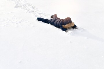 A child in a winter jumpsuit lies sprawled in full height in the snow, face down.