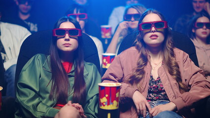 Obraz premium Shocked women watching film in cinema. Scared girl closing face in dark hall.