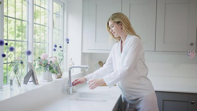 Pregnant woman wearing pyjamas standing in kitchen at home holding bump - shot in slow motion
