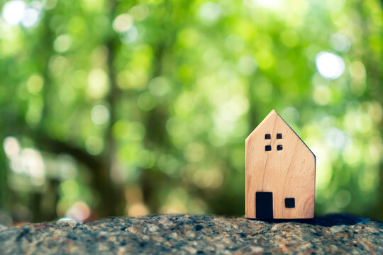 Closed up tiny home model on floor or wood board with sunlight green bokeh background. Deam life have own house property for living or investment.