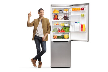 Casual man in checkered shirt and jeans leaning on a fridge and pointing up