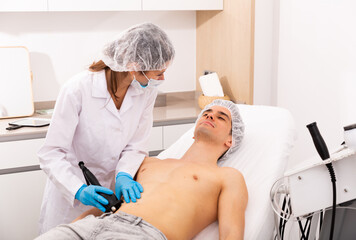 Young man receiving fat reductive skin lifting body treatment on modern equipment at cosmetology...
