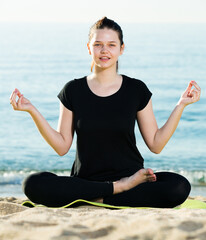 Female in black T-shirt is sitting and practicing meditation on the beach.