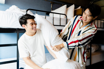 Asian men having fun playing pillow fight in dormitory bedroom.