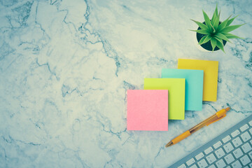 Four Color Stick Note or Notepad and Computer Keyboard and Office Plant and Pen on Modern Clean Marble Office Desk or Office Table Background in Vintage Tone