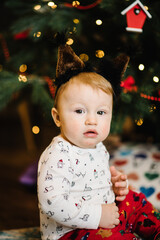 Cute baby boy wearing christmas suit crawling on floor over Christmas lights. Looking at camera. Holiday season.