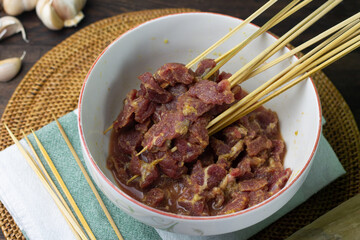 Preparation food to make Sate Daging or Indonesian popular Beef satay, beef slices marinated on ceramic white bowl, and some bamboo skewer. Beef satay usually make during Idul Adha celebration. 