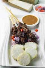 Sate Daging or Indonesian Beef Satay served on ceramic white plate, with slices of lontong, chilies, shallot and peanut sauce. Usually served on Idul Adha celebration. Isolated white background.  