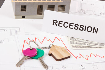 Keys, inscription recession, dollars and downward graphs representing financial crisis of real estate market. Reduced housing prices. House under construction