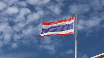 Thai flag on top flagstaff. The Thai national flag is waving in beautiful waves with the wind. On the blue sky background there are thin white clouds. selective focus