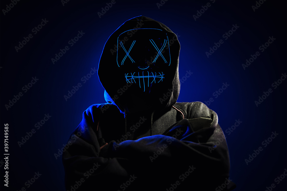 Wall mural Anonymous man in hoodie hiding face behind neon glow scary mask on dark background. Horror concept - Wall murals