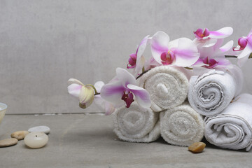 Concept for spa salon,with  rolled towel and branch orchid.,with candle ,stone on gray background, Copy space