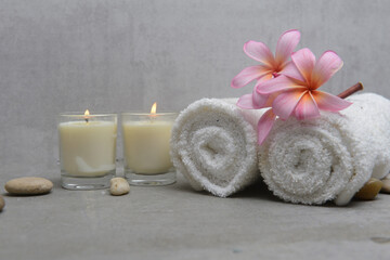 Fototapeta na wymiar Spa setting with plumeria flowers, candles and gray stones and rolled towel on gray background 