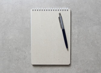 A spring notebook with a sheet of craft paper A5 with a ballpoint pen on light grey concrete background. Concept of new idea. Empty space for text
