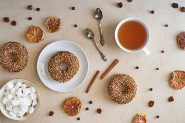 Breakfast ideas. Chocolate donuts, tea cup, tea spoons, sugar cubes, dried oranges and berries on beige background.