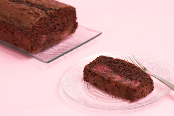 chocolate cake on pink background, slice on a transparent plate and the cake on a transparent tray