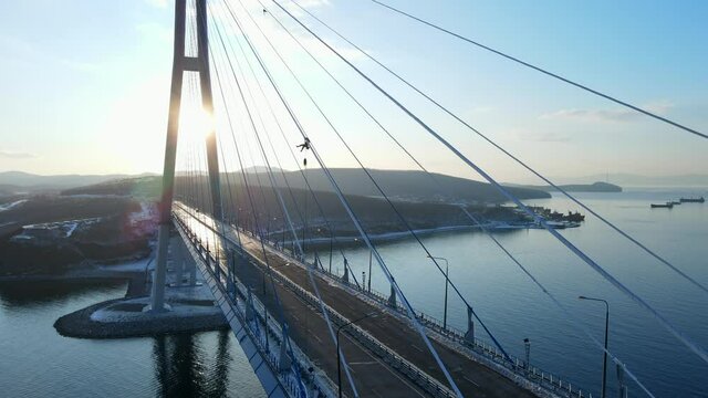 View from above. The silhouette of an industrial climber hanging on the icy shrouds of the Russian Bridge and clearing them of the ice crust. A worker hangs over a blocked road on a bridge