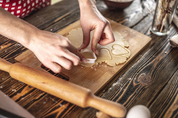 Fototapeta na wymiar Woman making delicious homemade cookies in the shape of heart in her kitchen. Concept of fresh homemade cakes or a surprise for Valentine's day