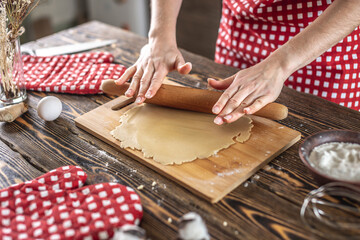 Woman is rolling out raw dough on a wooden table with a rolling pin to make delicious homemade cookies in her kitchen