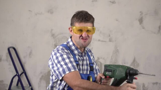 Funny crazy man construction worker shoots from an electric hammer perforator