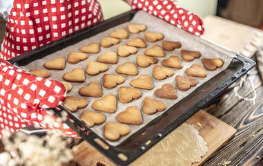 Woman is holding in her hands a baking sheet with delicious homemade cookies in the shape of a heart. Concept of fresh homemade cakes or a surprise for Valentine's Day