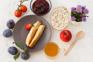 Homemade pancakes filled with cottage cheese on a plate, fruits and a cup of tea