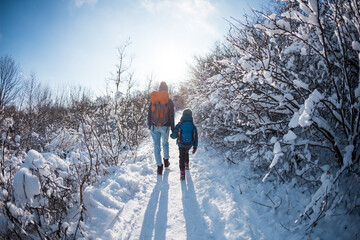 A child with a backpack walks with mother in a snowy forest