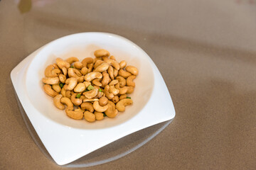 Tasty cashew nuts in plate on wooden table. white plate with cashew nuts on wooden table. Roasted cashew nuts 