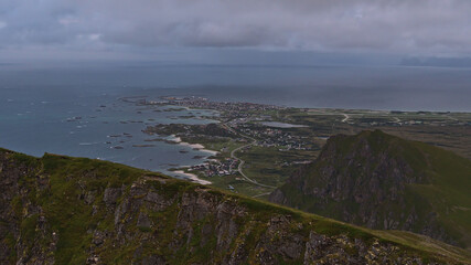 Panoramic view of fishing village Andenes located on the shore of Norwegian Sea in the north of Andøya island, Vesterålen, Norway with airfield and rugged mountains on cloudy summer day. 