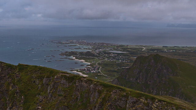 Panoramic view of fishing village Andenes located on the shore of Norwegian Sea in the north of Andøya island, Vesterålen, Norway with airfield and rugged mountains on cloudy summer day. 