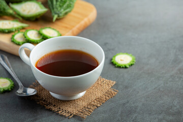 a cup of hot bitter gourd tea with sliced raw bitter gourd place on dark floor