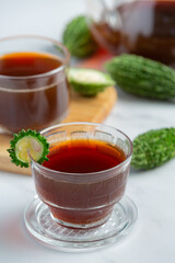 cups of hot bitter gourd tea with raw sliced bitter gourd on white marble floor