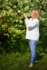 Outdoor portrait of a beautiful blonde middle-aged woman near blossom apple trees with white flowers.