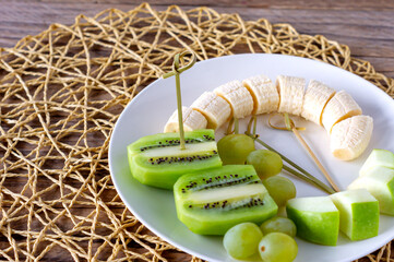 Vegan breakfast- variety of fruits. Apples, bananas, kiwi and grapes on a plate on the grey wooden table, selective focus, fruit salad