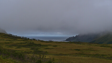 Mystic view of the northwestern coast of Andøya island, Vesterålen in northern Norway near village Bleik with rugged mountains vanishing in the low clouds and green colored meadows and forests.