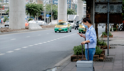 Female tourists are waiting for a taxi in the city by using the application in the smartphone to call a car