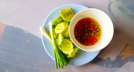 Top view of fresh slice cucumber, lime, spring onion and fish sauce with red and green chili in white bowl. Side dish of fried rice and flat lay of freshness vegetable.