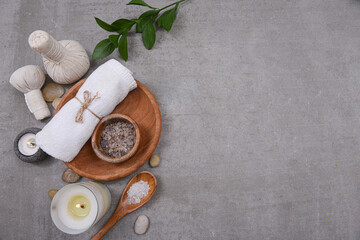 Fototapeta na wymiar Rolled towels and salt in bowl in wooden bowl, bamboo leaves,stone and,candle on grey background, Copy space for your text