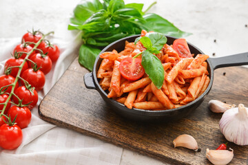 Frying pan with penne pasta and tomato sauce on light background
