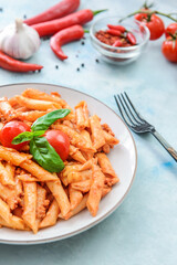 Plate of penne pasta with tomato sauce on light background