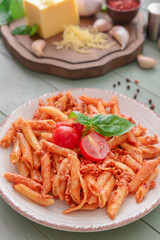 Plate of delicious penne pasta with tomato sauce on wooden background