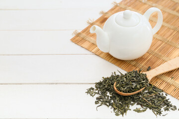 Spoon with dry green tea and teapot on light table