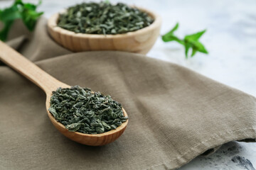 Spoon and bowl with dry green tea on table