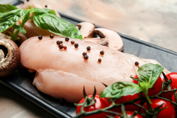 Board with raw chicken fillet, herbs and vegetables on table