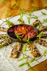 A circular composition on the table with homemade fruit leather pieces in the bowl and granola bars of seeds and nuts around i. Fresh, green spring sprouts in the vase. 